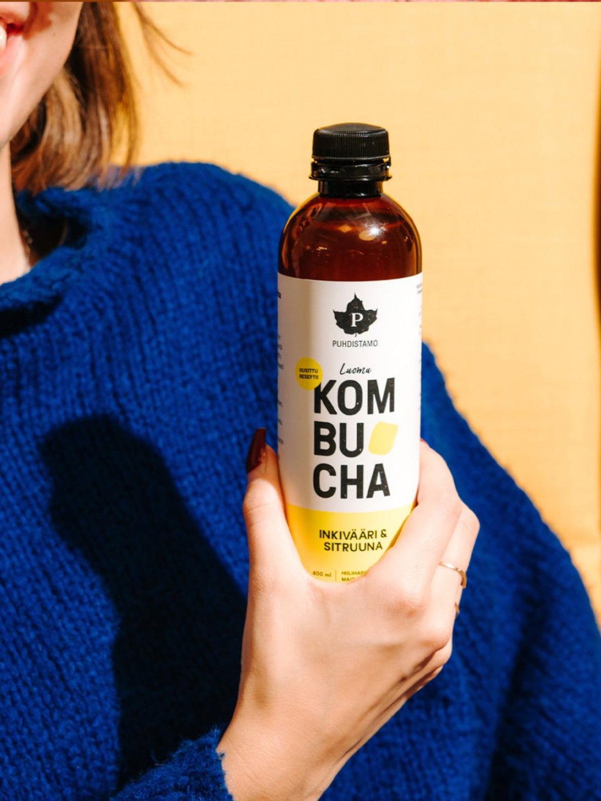 Nainen pitää kädessään Puhdistamon Luomu Kombucha inkivääri & sitruuna pulloa