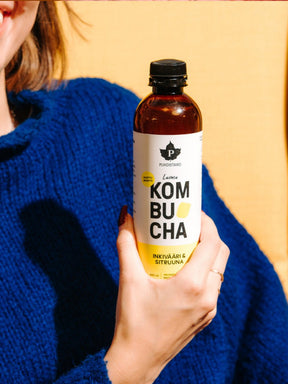 Nainen pitää kädessään Puhdistamon Luomu Kombucha inkivääri & sitruuna pulloa