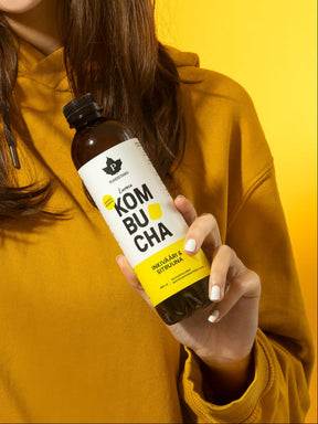 Nainen pitää kädessään Puhdistamon Luomu Kombucha Inkivääri-Sitruuna pulloa