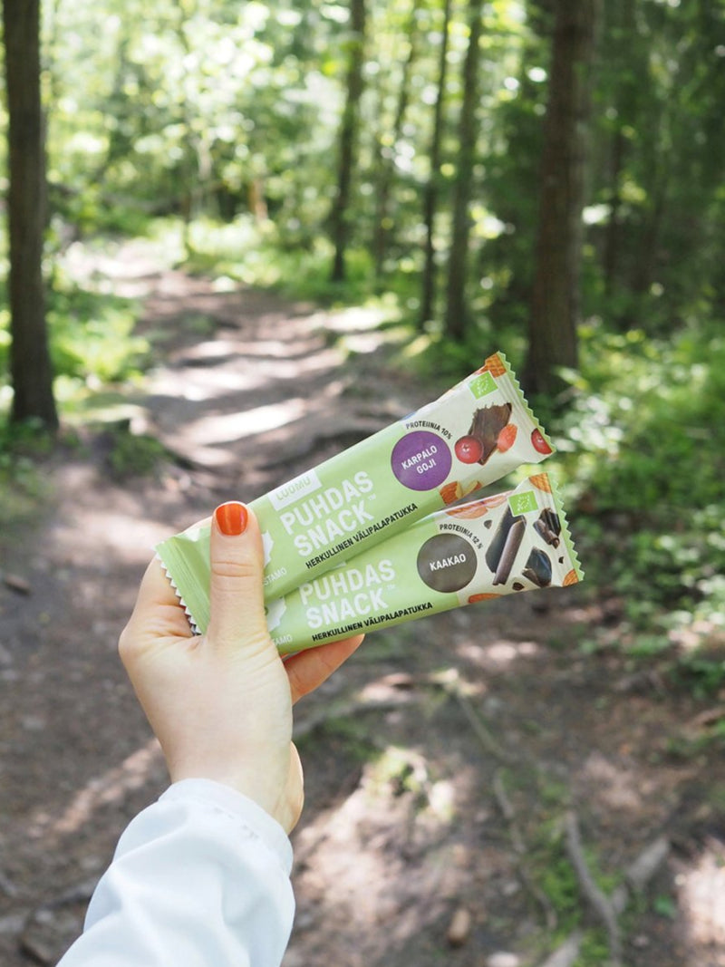 Nainen pitää kädessään kahta Puhdistamon Puhdas Snack™ patukkaa metsätiellä