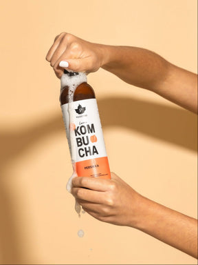 Nainen pitää kädessään kuohuavaa Puhdistamon Luomu Kombucha persikka pulloa